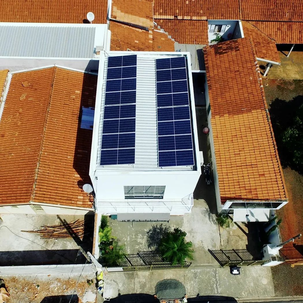 Vista aérea de uma casa branca com telhado colonial e módulos fotovoltaicos ocupando a face voltada para o sol