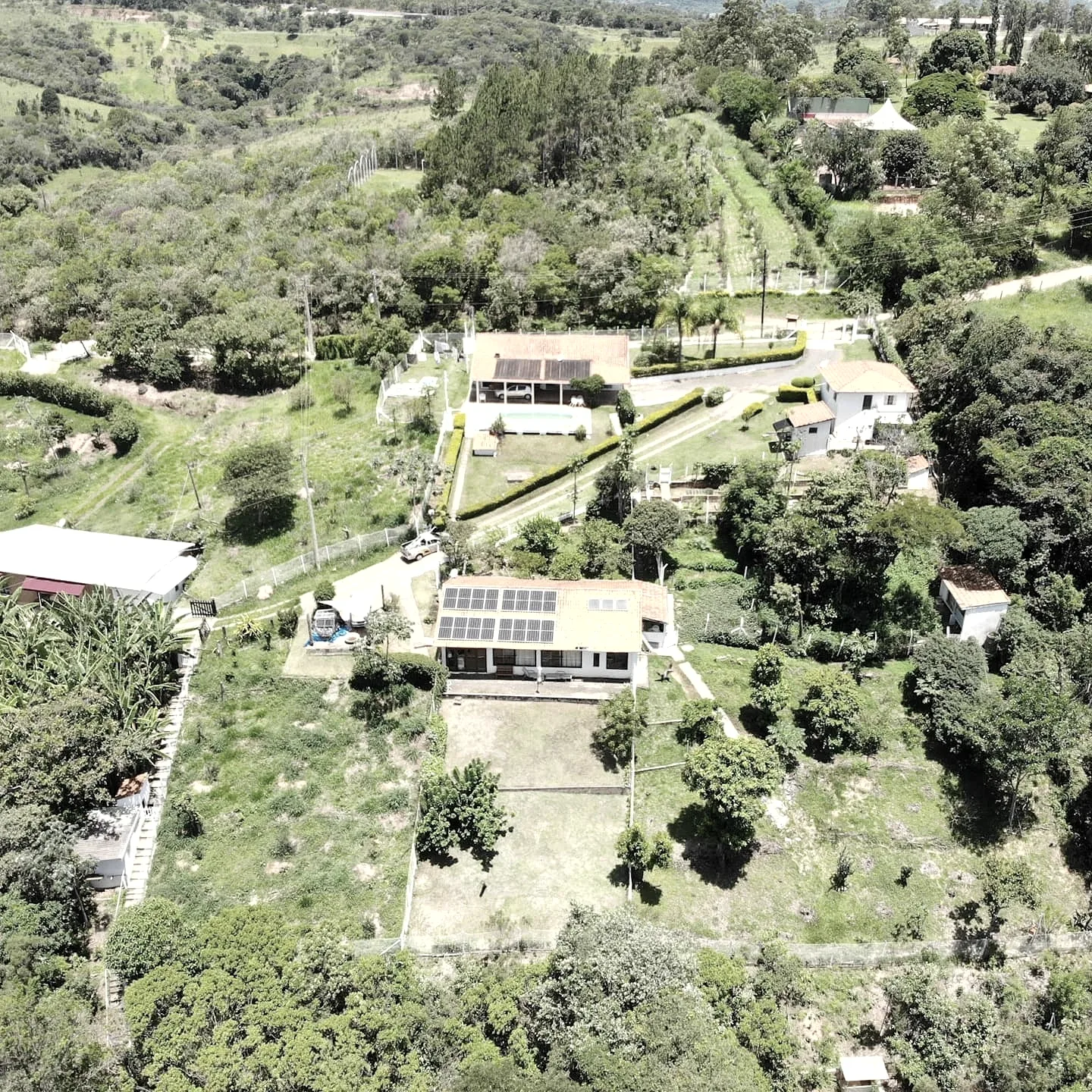 Vista aérea de propriedade rural com casas, área verde e módulos fotovoltaicos instalados em telhado