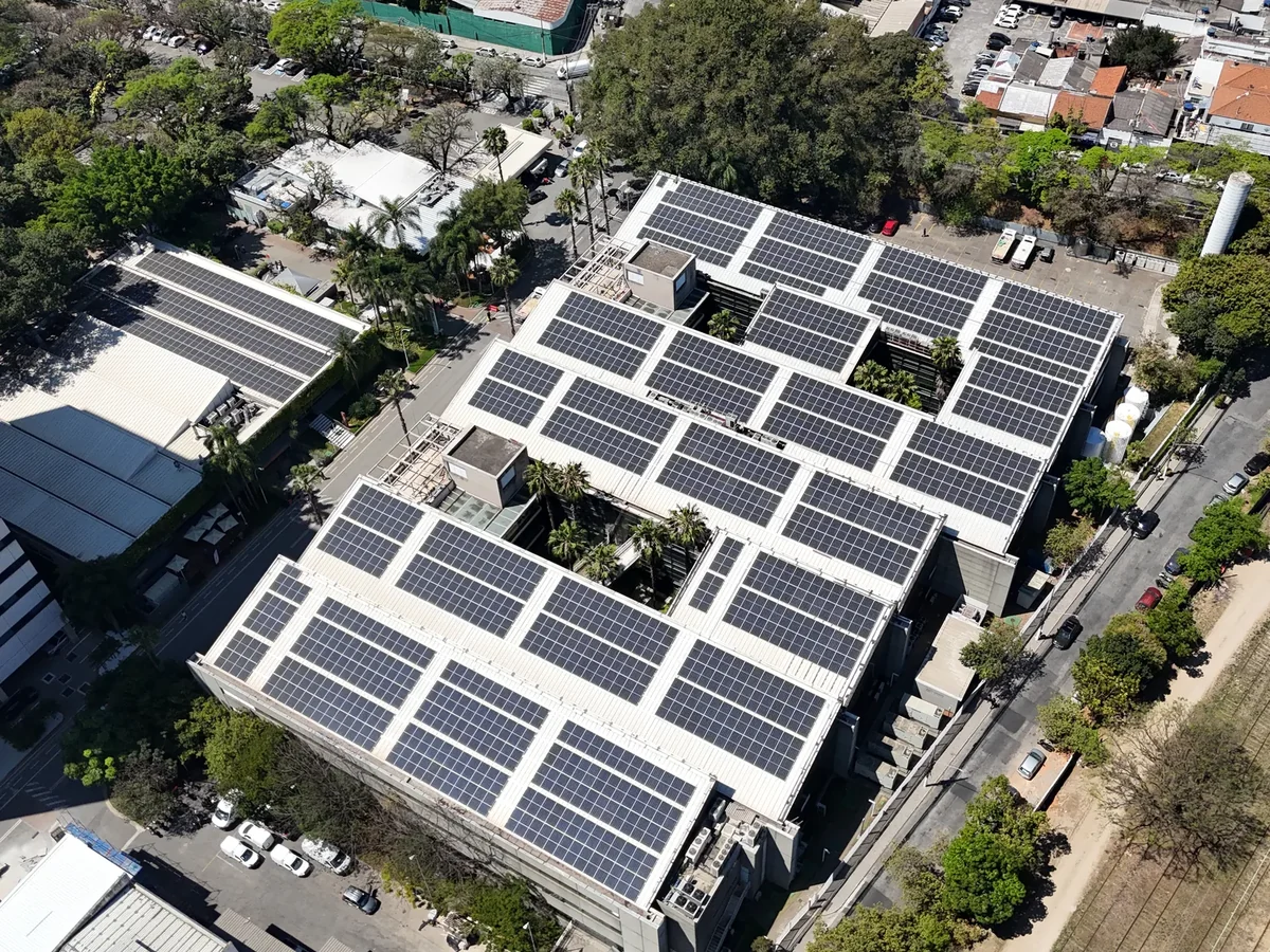 Vista aérea de cobertura de grande porte inteiramente ocupada por fileiras de módulos fotovoltaicos, em área urbana