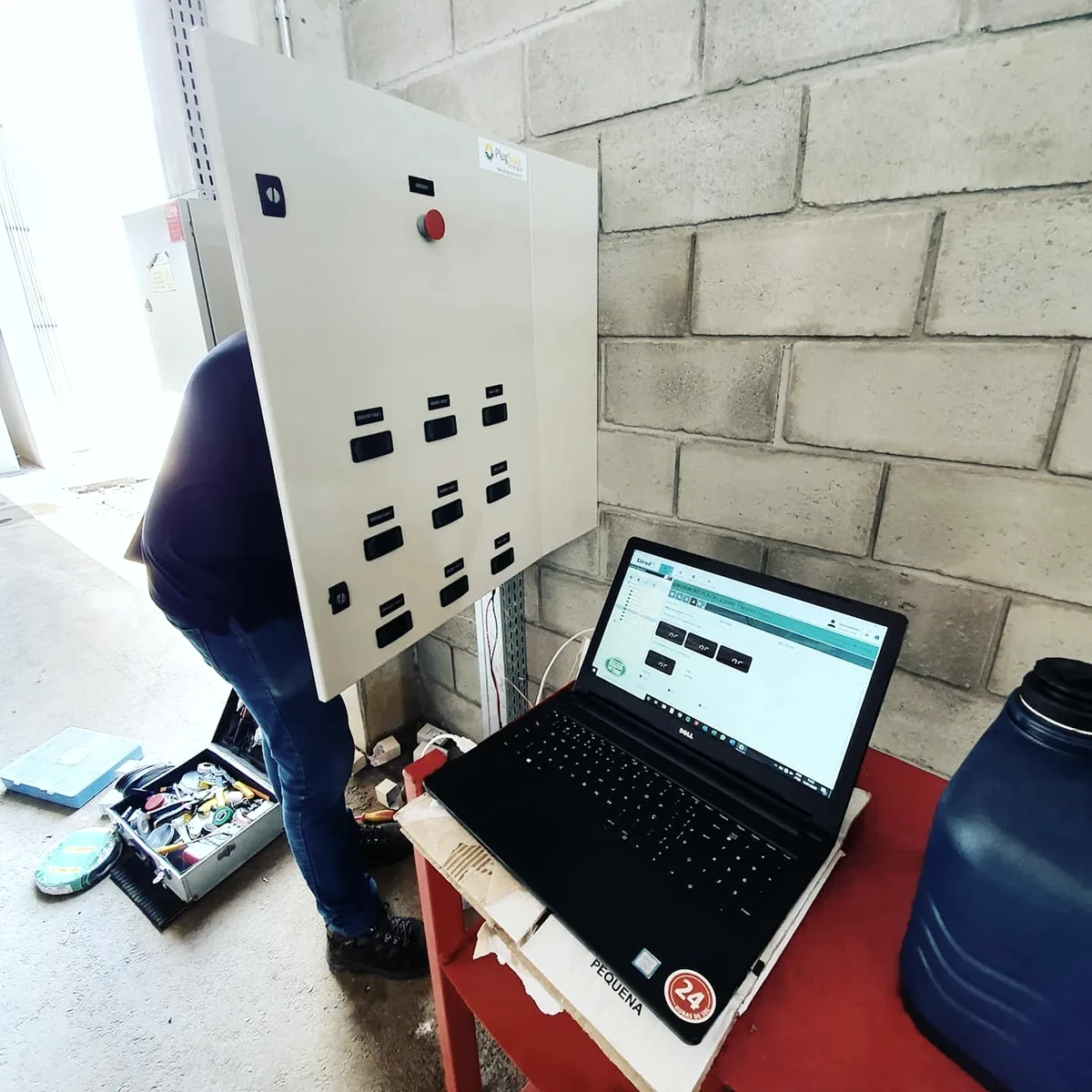 Profissional com notebook em frente a um quadro elétrico aberto, durante comissionamento