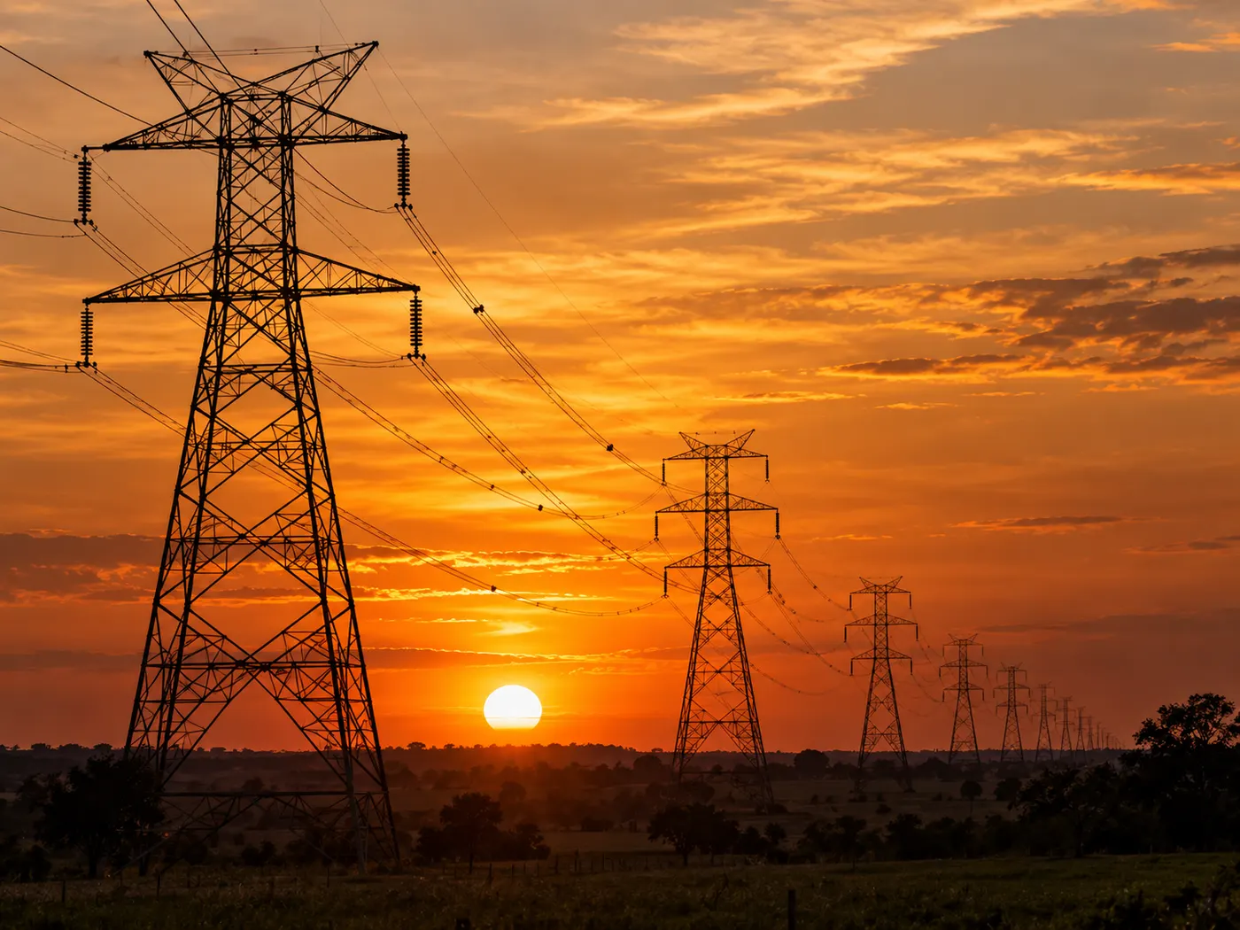 Torres de transmissão de energia elétrica de alta tensão em silhueta contra o céu alaranjado do pôr do sol
