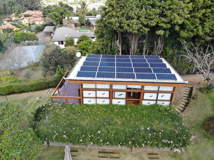 Casa de campo com módulos fotovoltaicos instalados no telhado, cercada por área verde