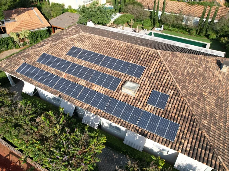 Casa de telhado cerâmico vista de cima, com módulos fotovoltaicos em fileiras e piscina ao fundo